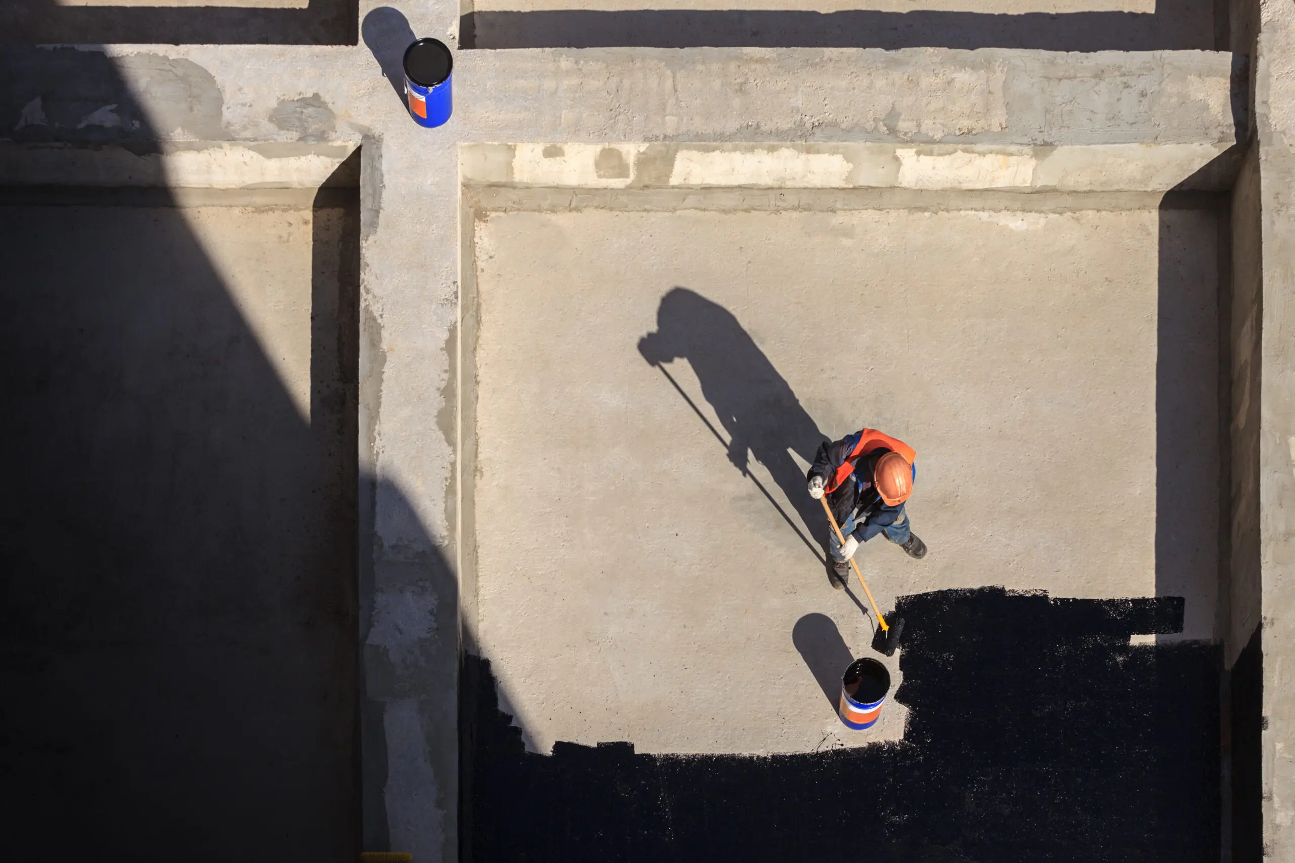 The worker in overalls applies an insulation coating on the concrete surface. View from above. The worker in overalls applies an insulation coating on the roof's surface. View from above.