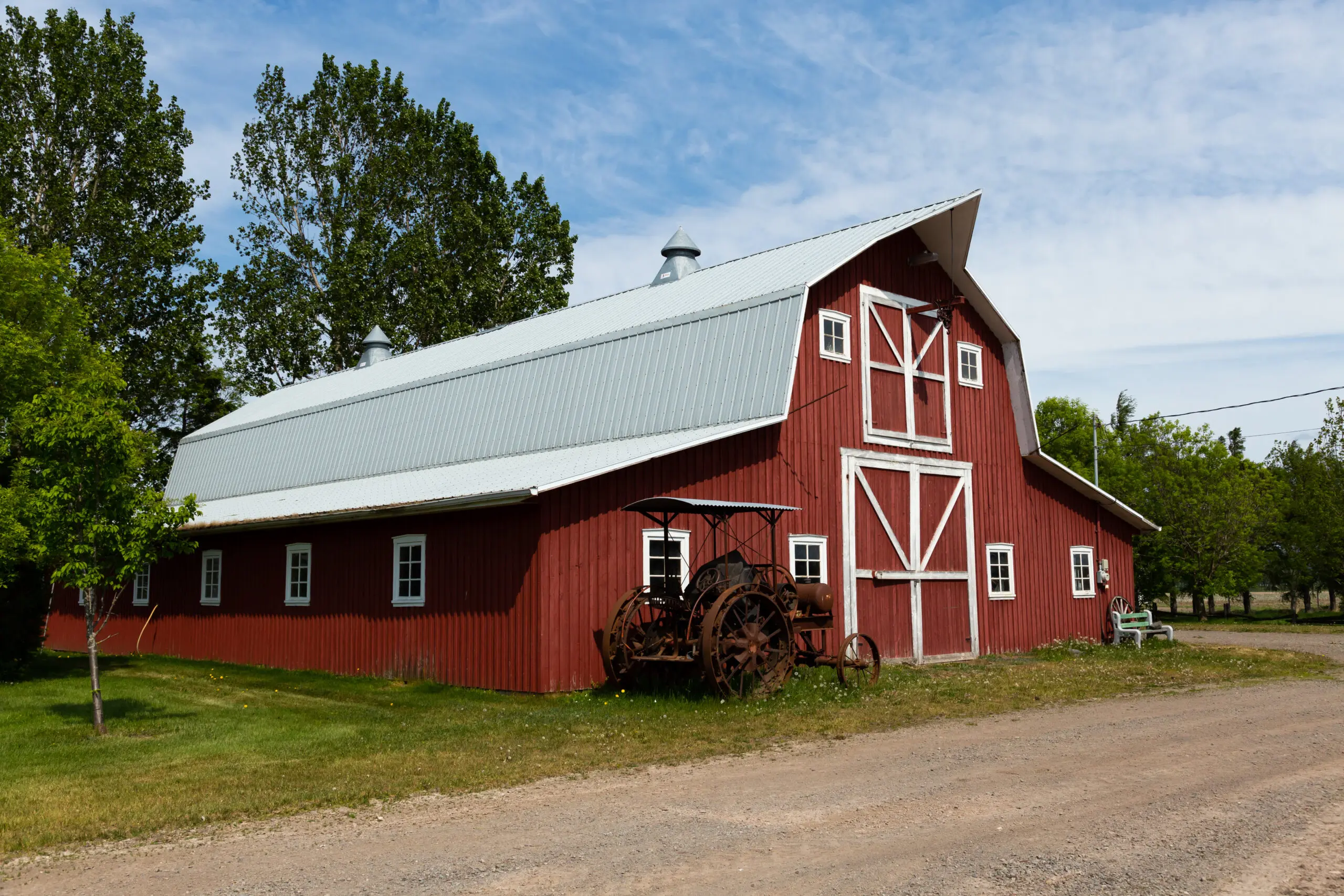 vintage rusted tractor in front of patrimonial red wooden barn with metal gambrel aluminum reflective coated roof