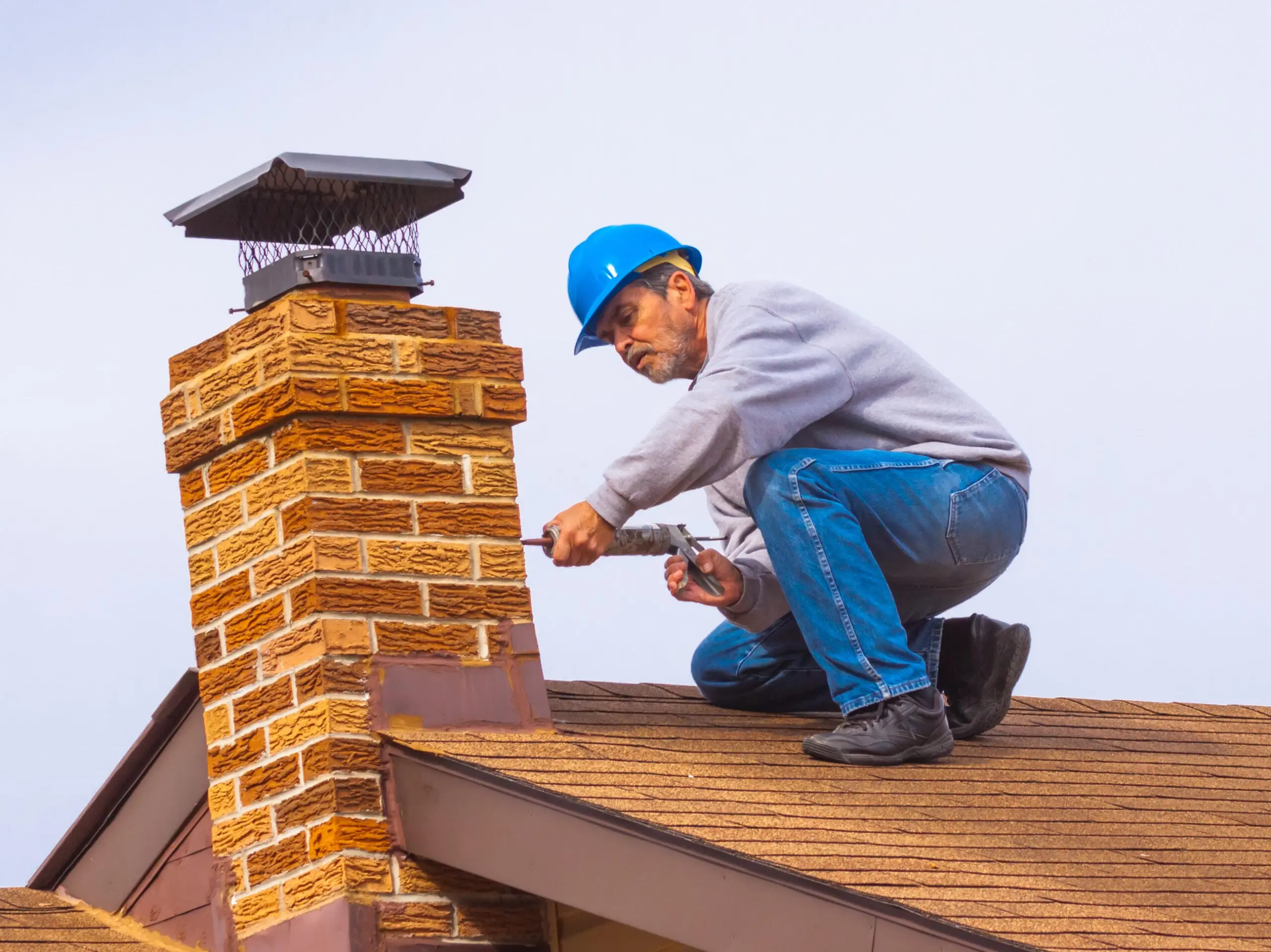 Contractor Builder with blue hardhat on the roof caulking chimney
